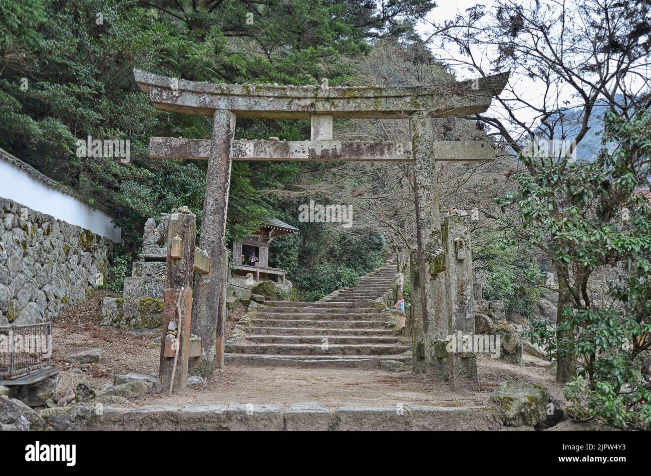 Old stone torii gate over a stairs path in forest park on Mount Misen in Miyajima, Hiroshima, Japan Stock Photo