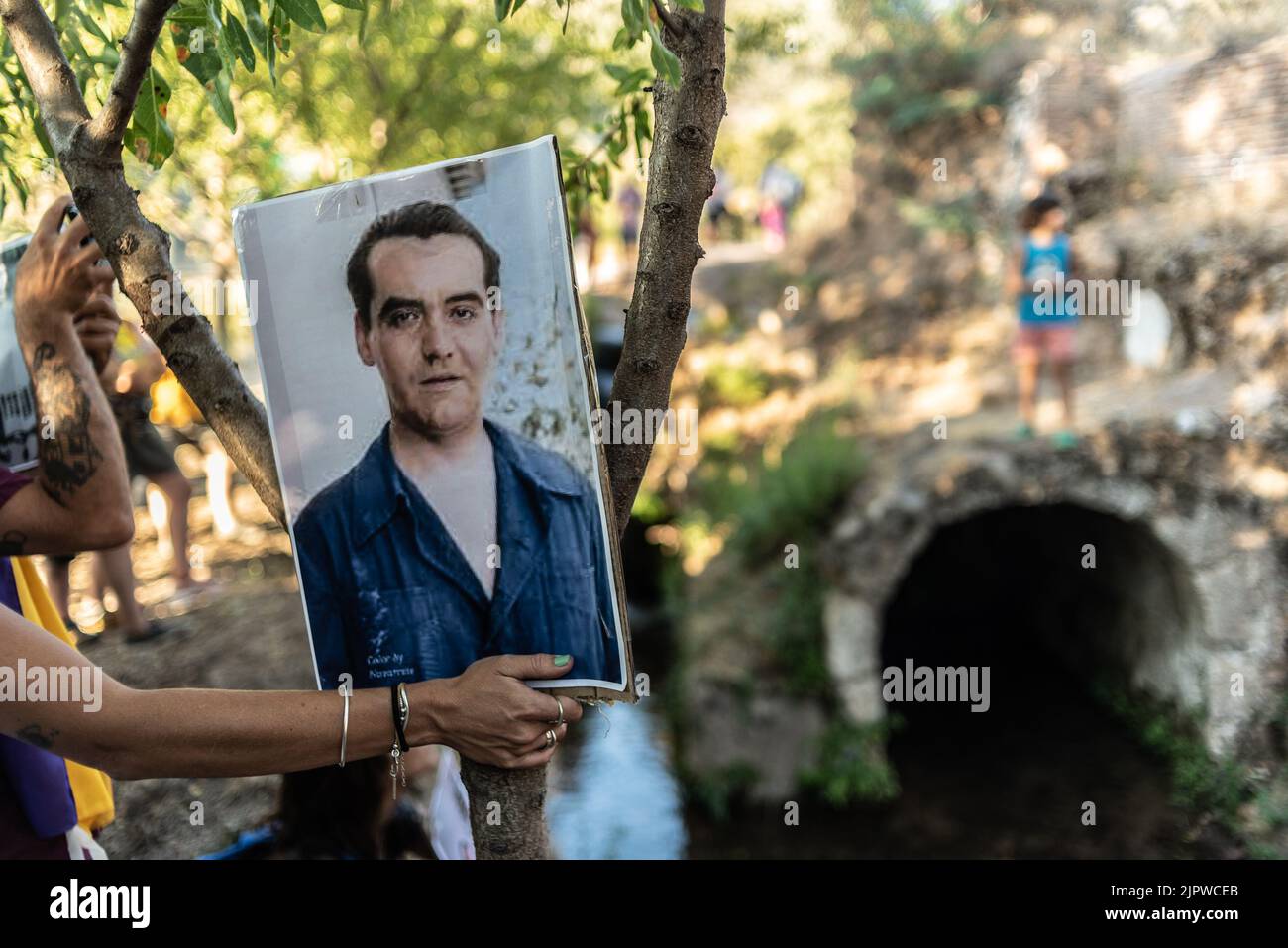 woman's hand holding a photograph of Federico Garcia Lorca in a Viznar forest in a place called La Colonia and in the background the outlet of an unde Stock Photo
