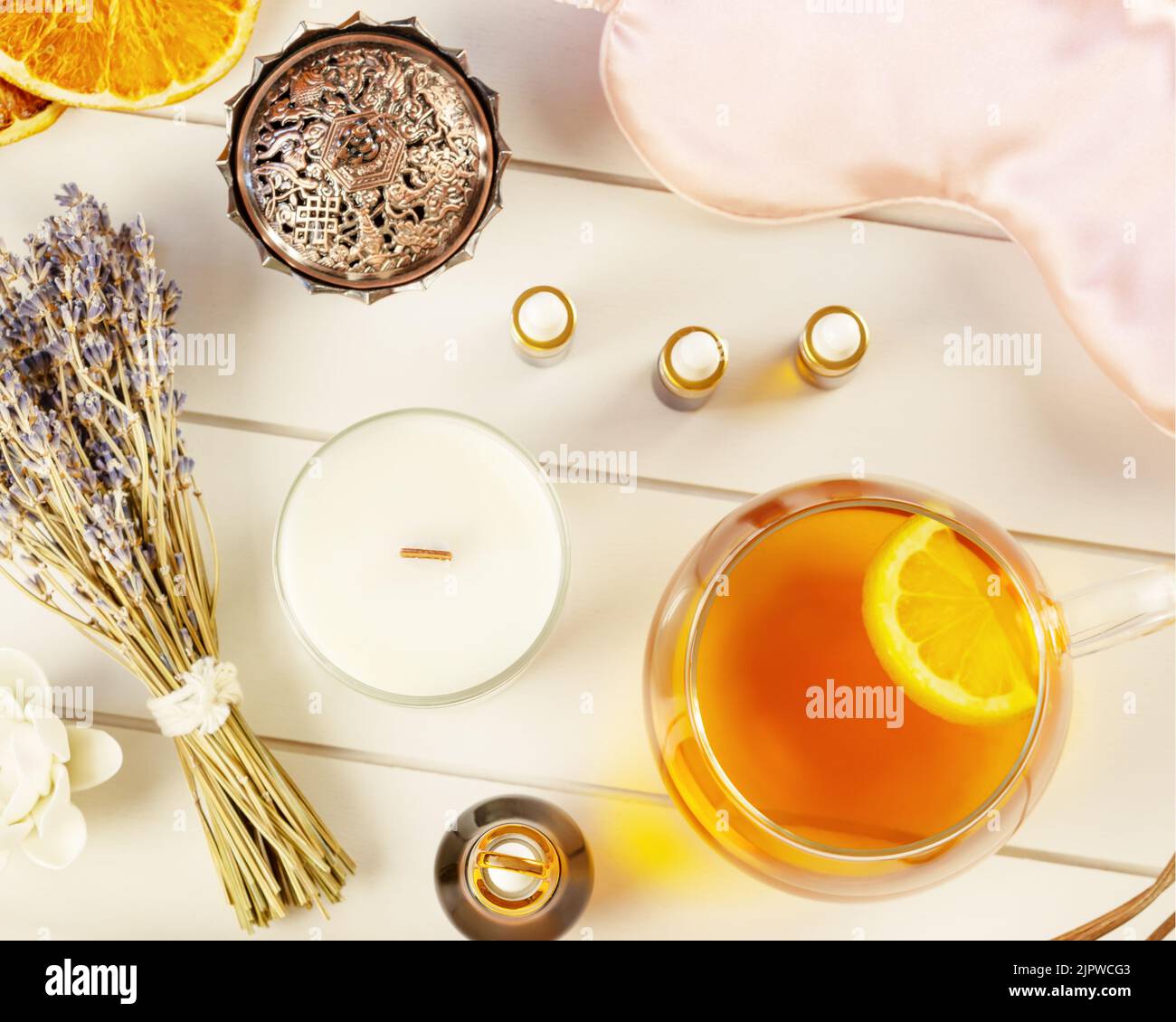 Relax at home. Cup of herbal tea, aroma candle, sticks, lavender flowers, dry oranges and natural oils on wooden background. Insomnia or depression tr Stock Photo
