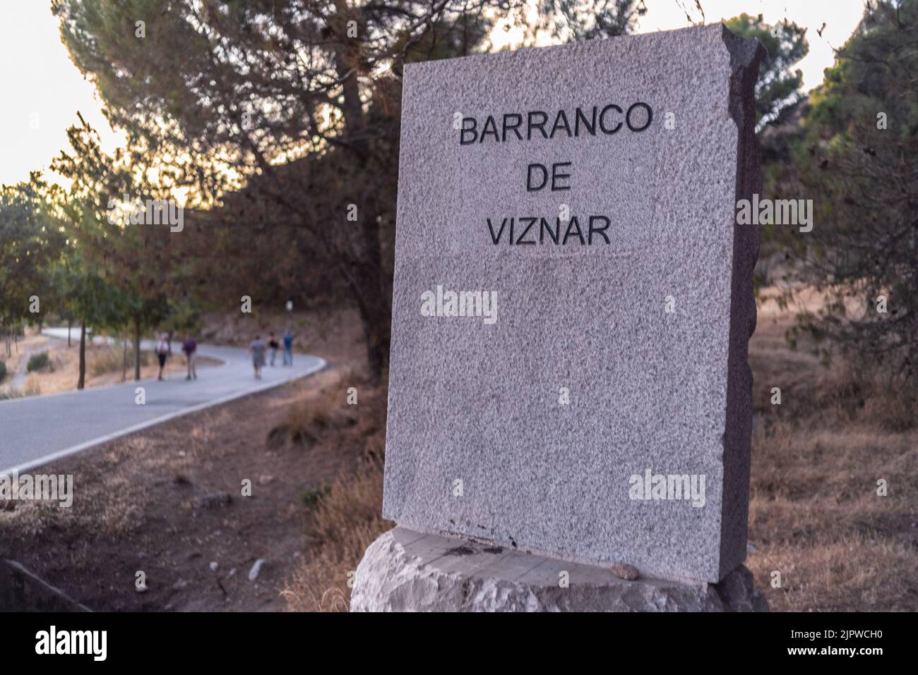 Monolith that reads ravine of Viznar next to the road that goes from Viznar to Alfacar with people walking along it Stock Photo