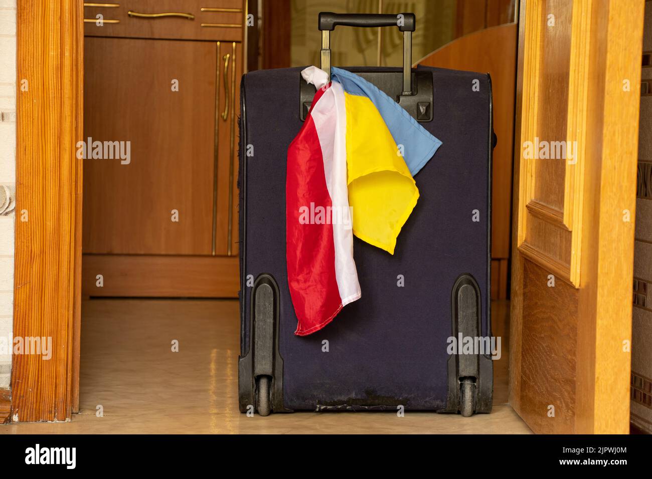 A suitcase with the flag of Poland and the flag of Ukraine stands in the corridor at the exit from the apartment in Ukraine, refugees in Ukraine leave Stock Photo