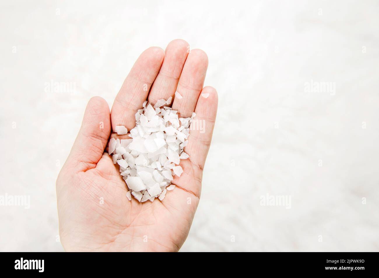 Close up view of person hand holding Magnesium Chloride vitamin salt flakes in palm, white minimal background, lot of copy space. Stock Photo