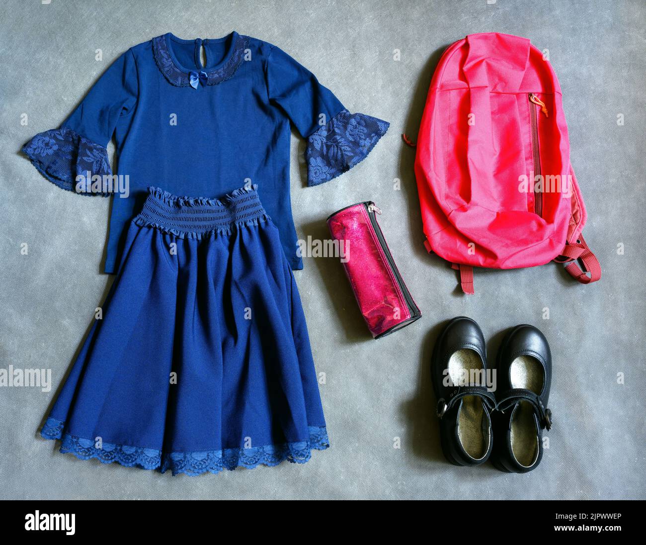 School uniform for little girl on gray background, flat lay. Top view of student clothes, set with shoes, skirt, shirt and backpack. Concept of first Stock Photo