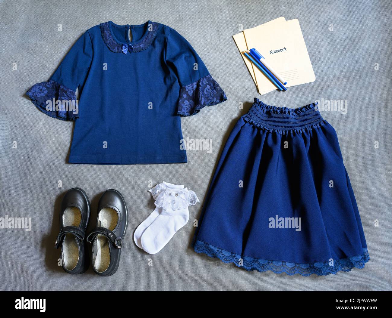 School uniform for little girl on gray background, flat lay. Top view of student clothes, set with shoes, skirt, shirt and notebooks. Concept of first Stock Photo