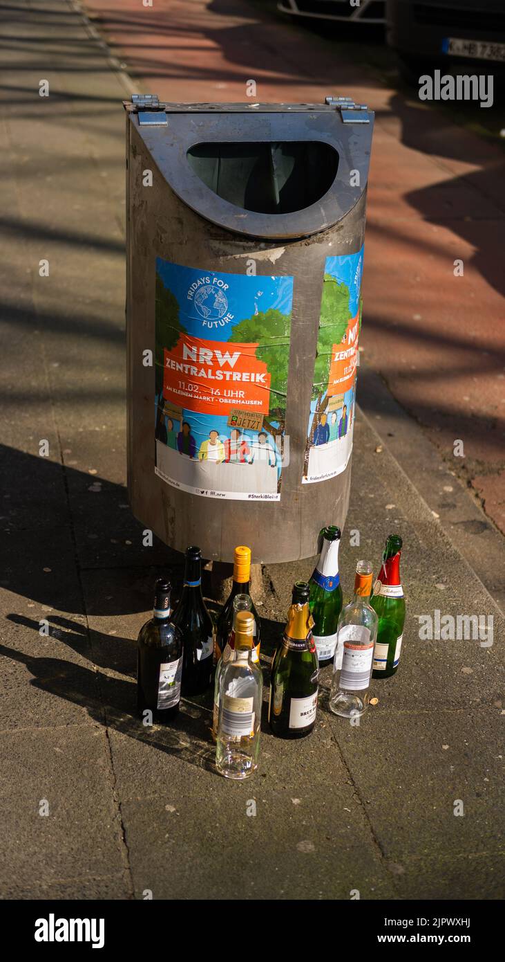 A vertical shot of an alcohol glass waste in front of trash bin with