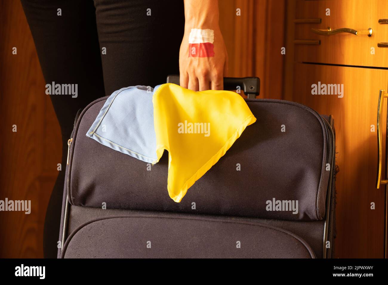 A girl with a suitcase with the flag of Poland and the flag of Ukraine leaves home because of the war in Ukraine, Ukrainian refugee leaves home with a Stock Photo