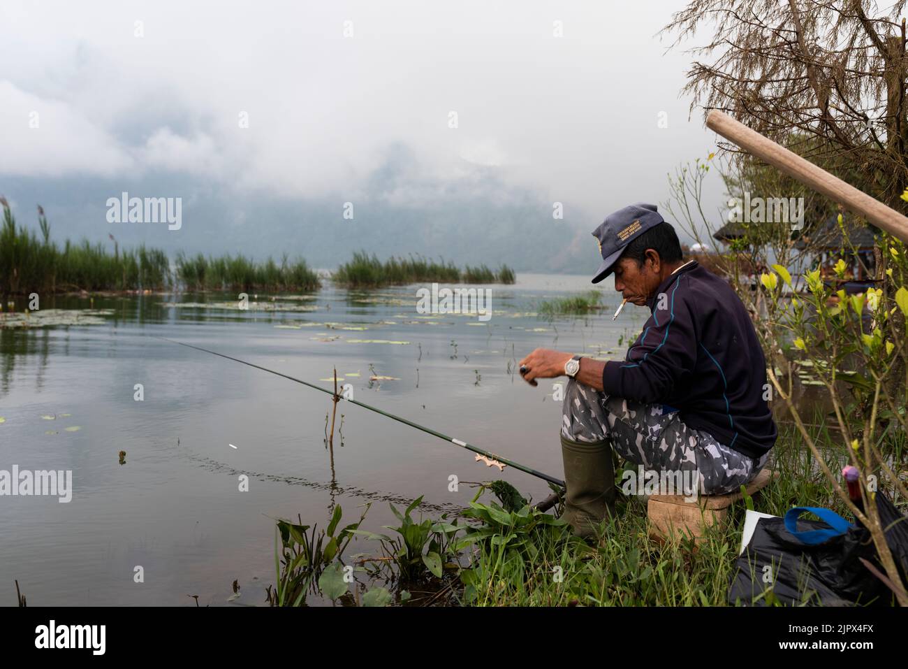 UBUD, BALI, INDONESIA, MAY 15, 2017; Portrait of old man fishing by Danau Bratan lake. Indonesian man image. Stock Photo