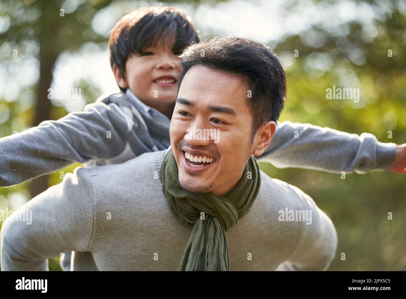 young asian father carrying son on back having fun enjoying nature outdoors in park Stock Photo