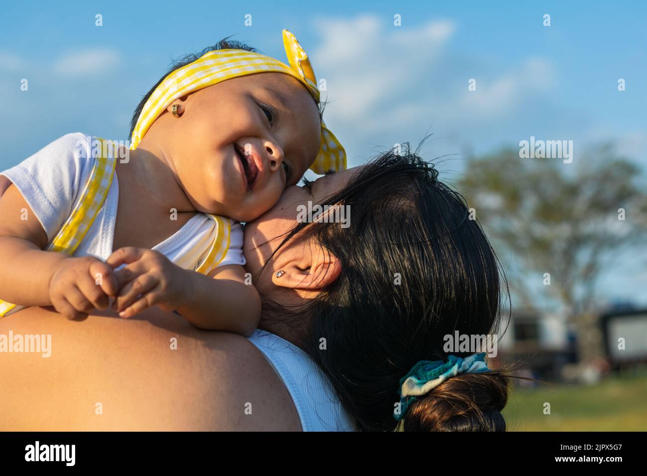 close-up of a beautiful latin baby girl being held by her mother, nodding her head, smiling and holding her cheeks together, giving affection to each Stock Photo