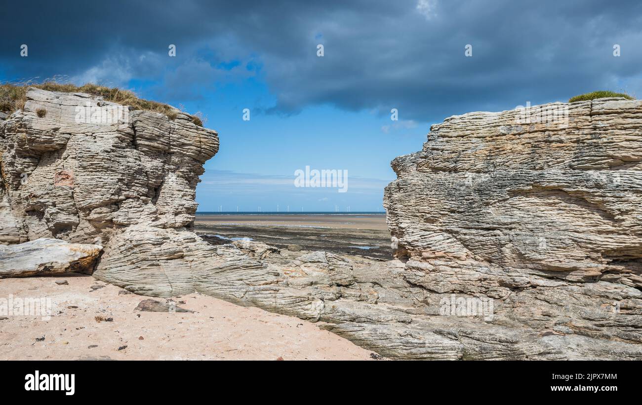 A window rock formation seen at Hilbre Island frames the wind turbines off the Wirral penninsula in the Irish Sea. Stock Photo