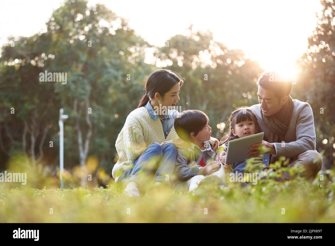 asian family with two children relaxing outdoors in city park Stock Photo