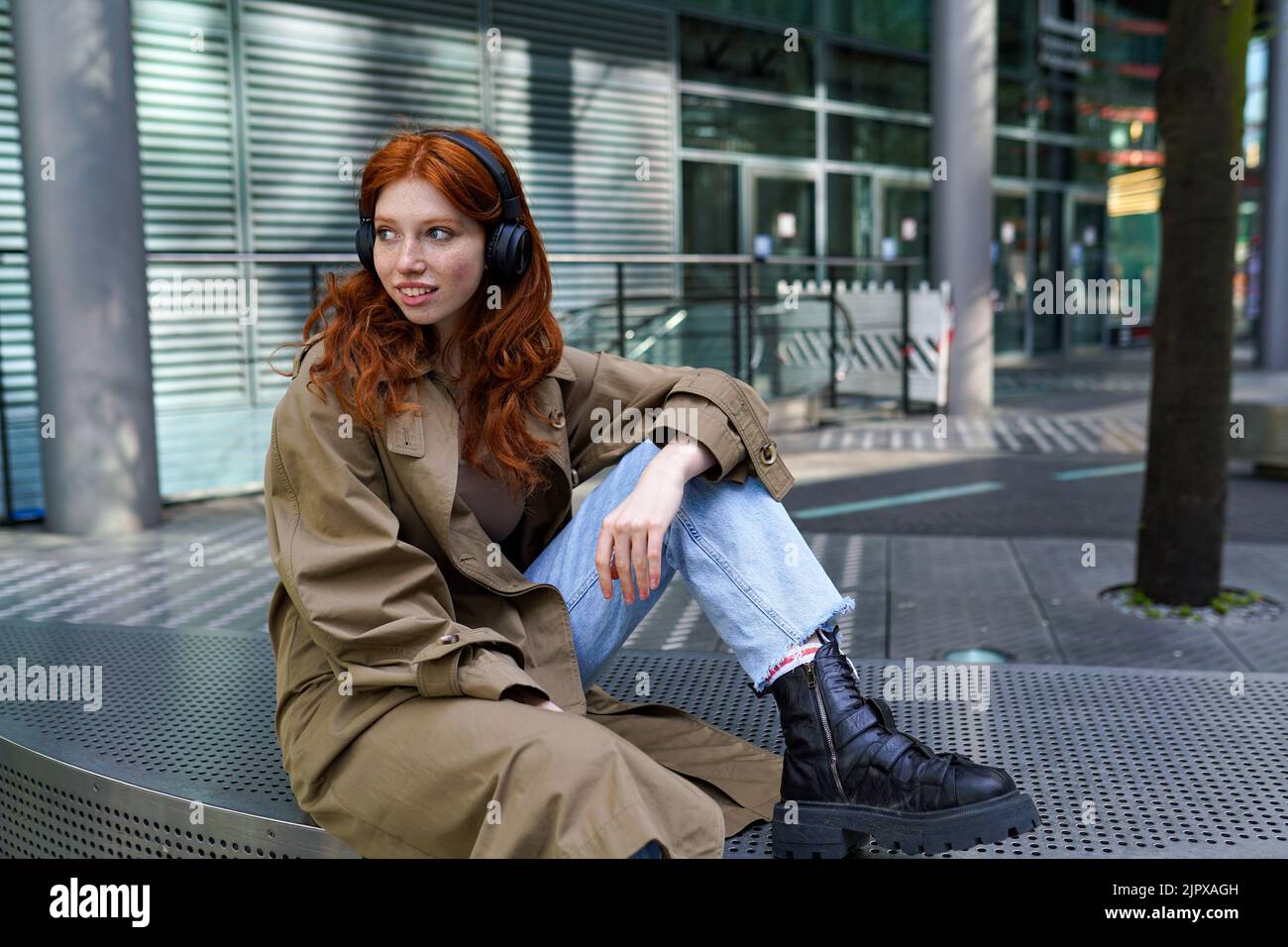 Smiling teen redhead hipster girl wearing headphone listening music in the city. Stock Photo