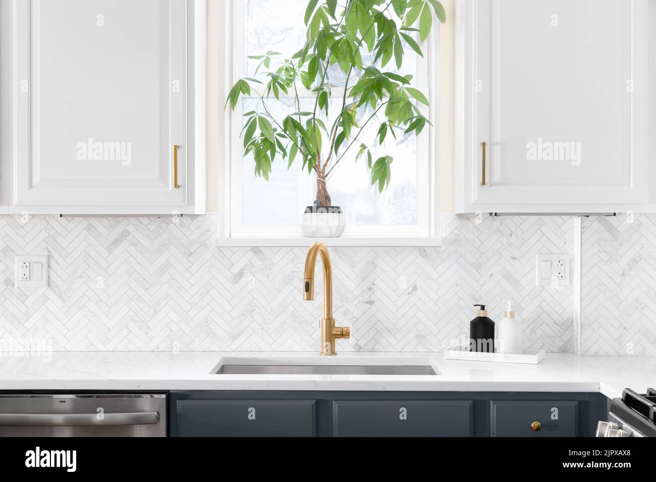 Sink detail shot in a luxury kitchen with herringbone backsplash tiles. white marble countertop, and gold faucet. Stock Photo