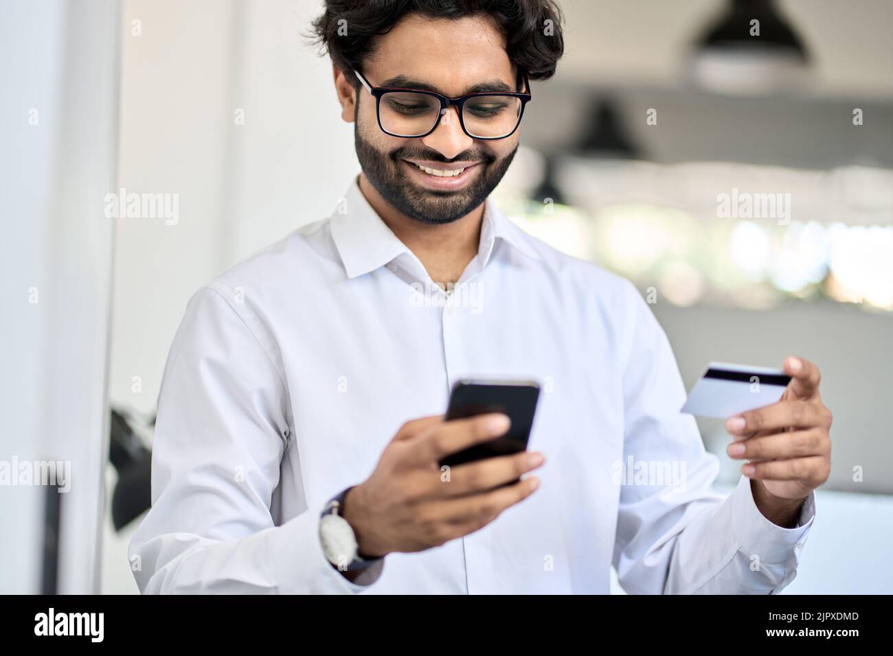 Happy indian business man holding phone and credit card using mobile bank app. Stock Photo