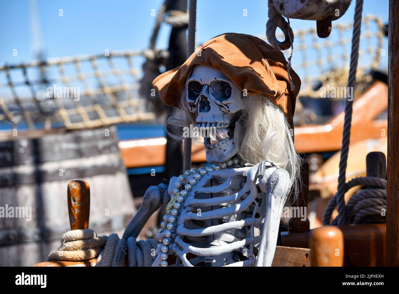 Spooky mock up pirate skeleton wearing a hat and a pearl necklace on a traditional sailing ship. Stock Photo