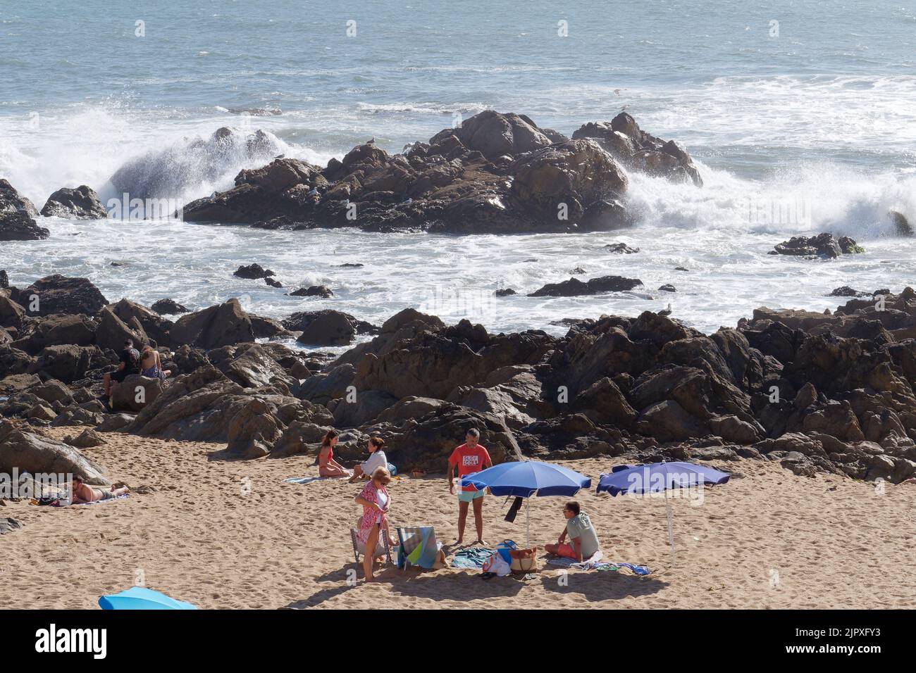 Family enjoying a day on the Foz do Douro beach in the Porto area of Portugal. Waves crash over the rocks as the family sit and relax. Stock Photo
