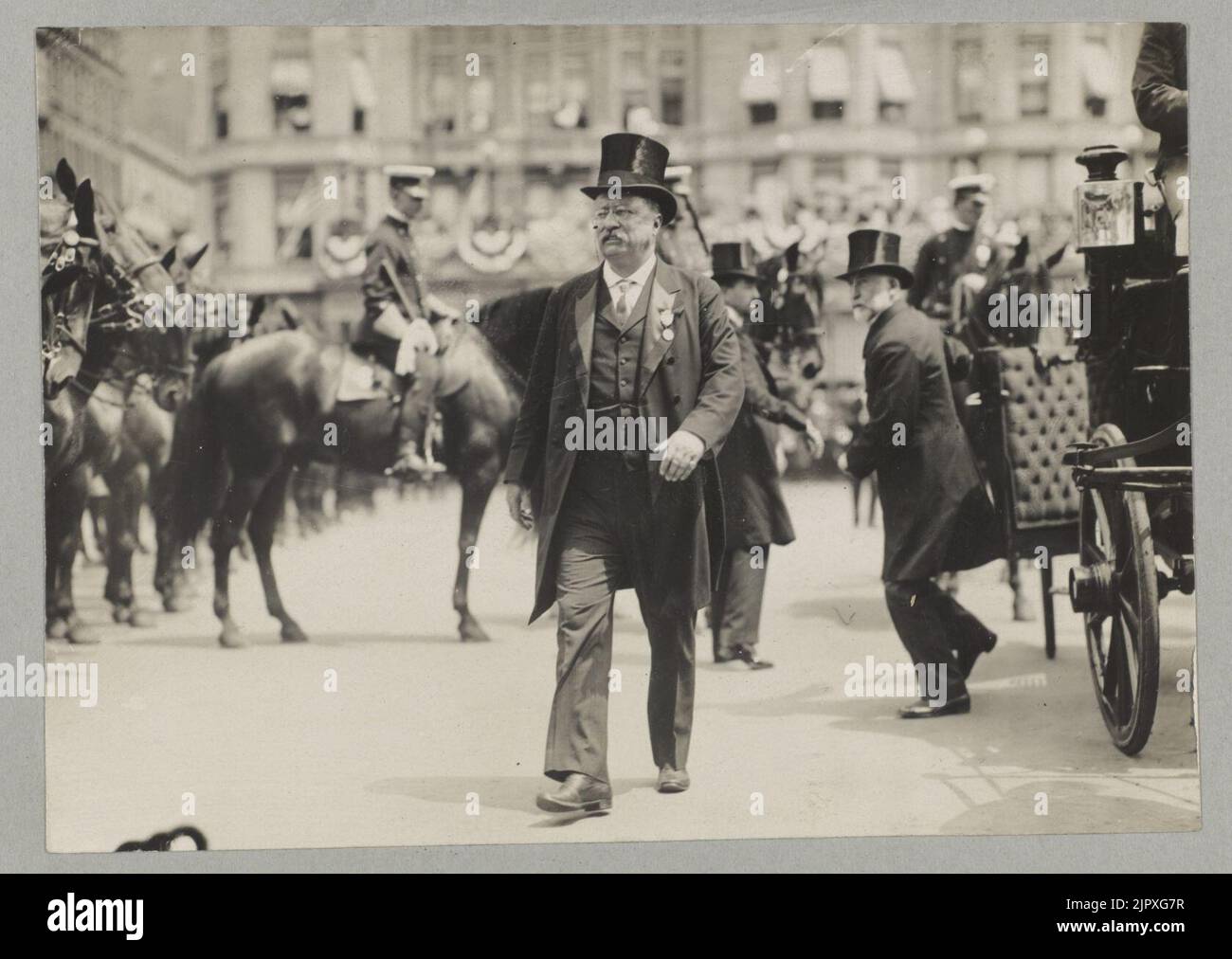 Theodore Roosevelt walking in top hat, tails, and medal; with men