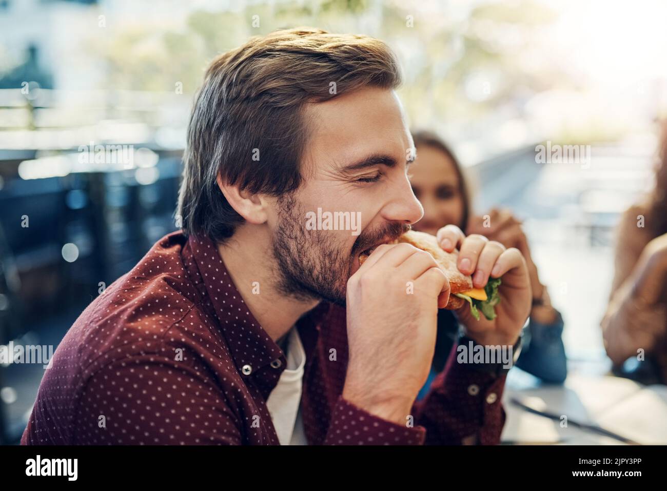 The first bite is always the best. a handsome young businessman enjoying his sandwich while having a breakfast meeting outside. Stock Photo