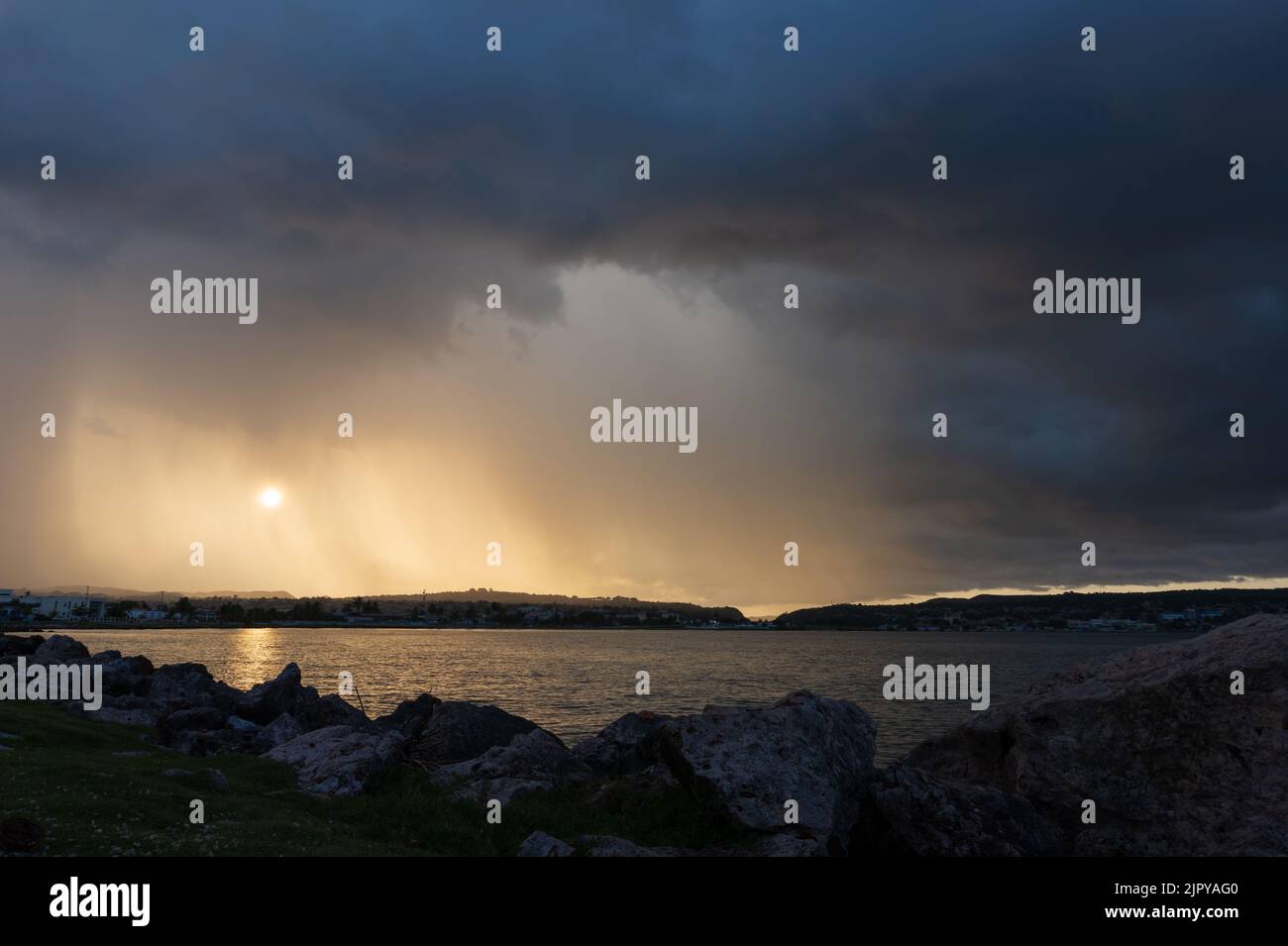 Sunset in the Matanzas bay in the summer with the sun reflected in the water and rocks in the foreground. Stock Photo