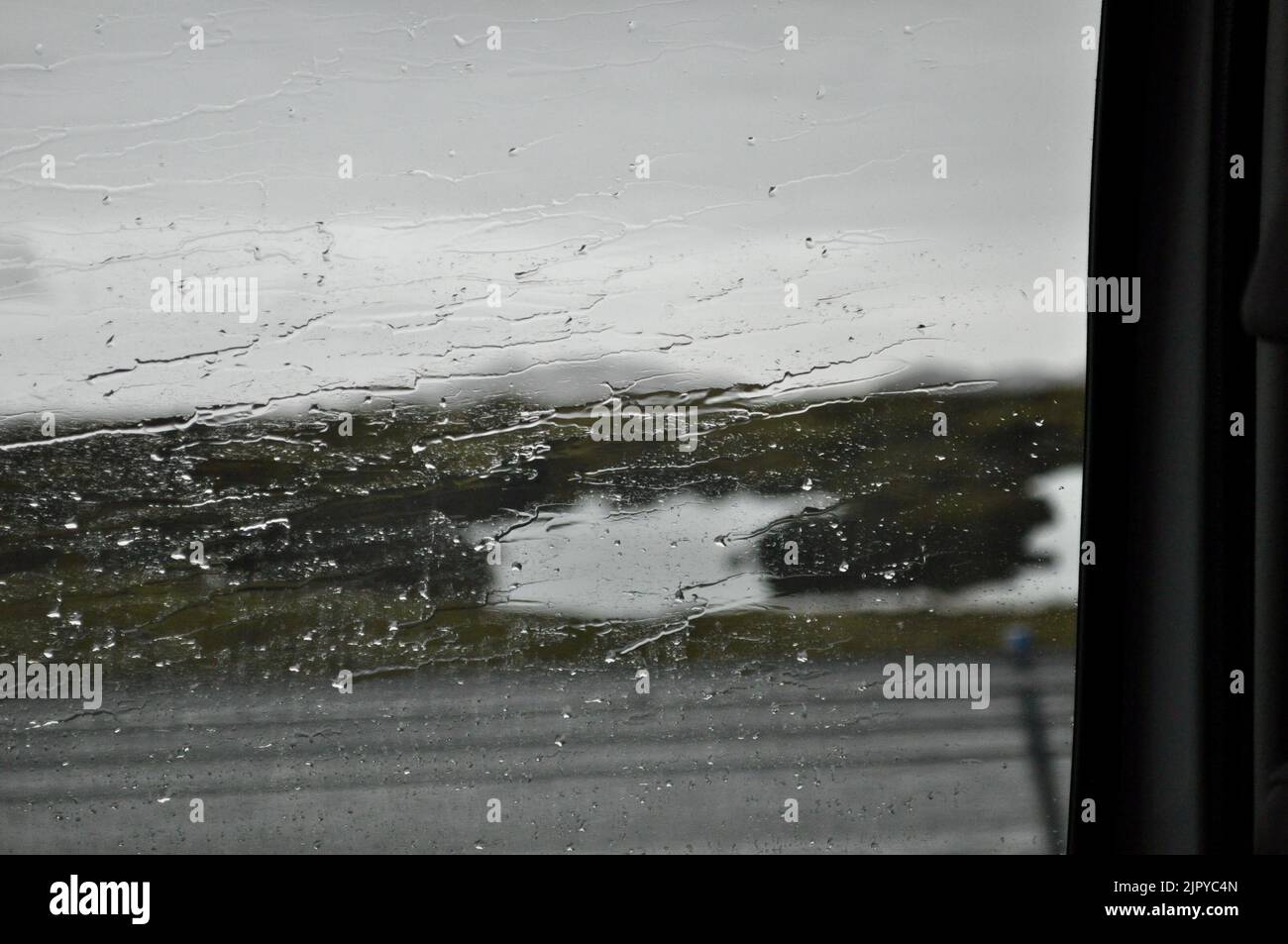 Rain streaks a car window while passing the beautiful landscapes of
