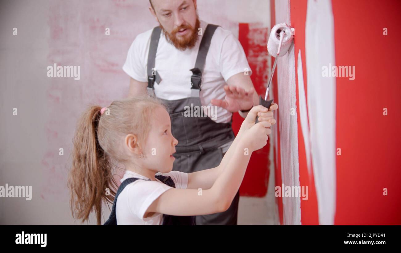 A little girl painting wall with a paint roller - her dad watching her Stock Photo