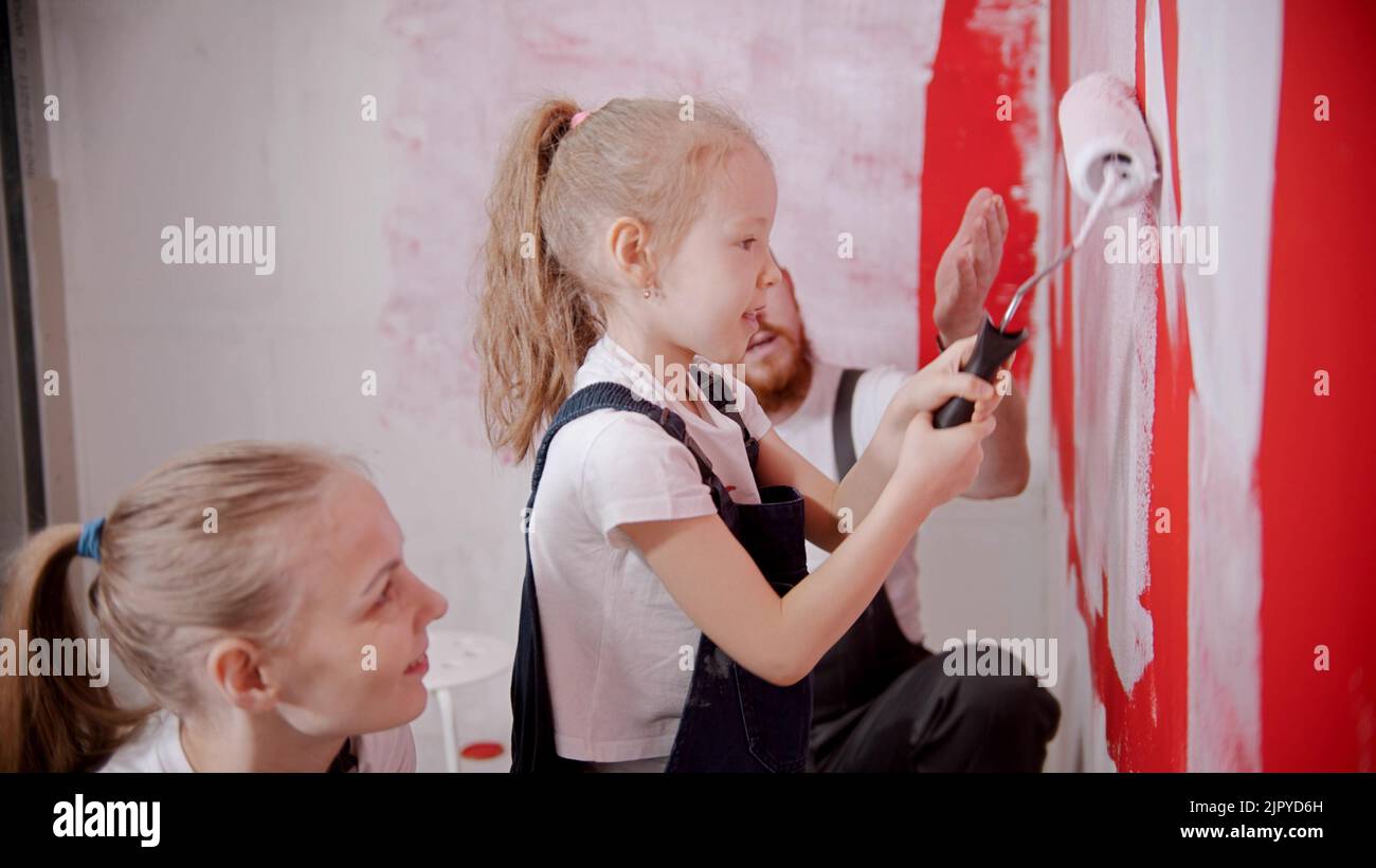 Mom and dad teaching his little daughter how to paint walls correctly Stock Photo
