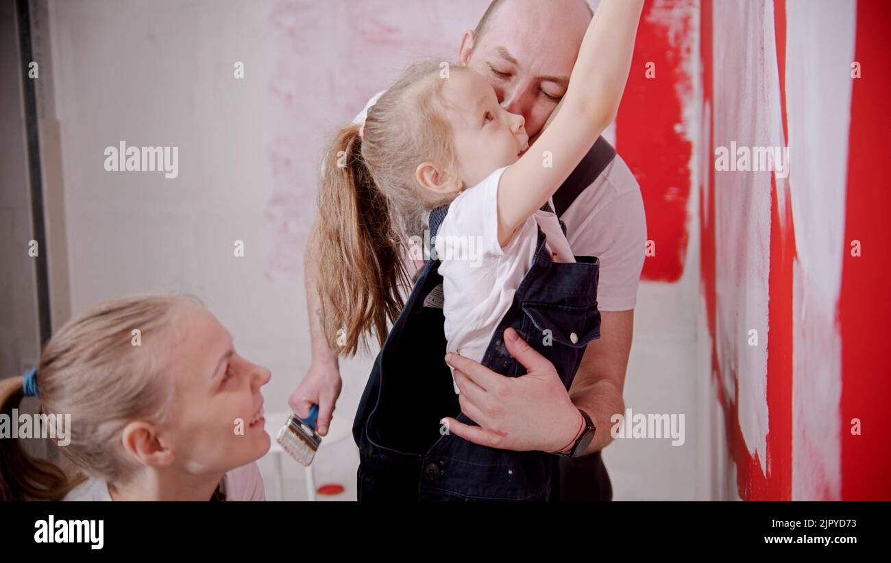 Mom and dad teaching his little daughter how to paint walls - raise her higher Stock Photo