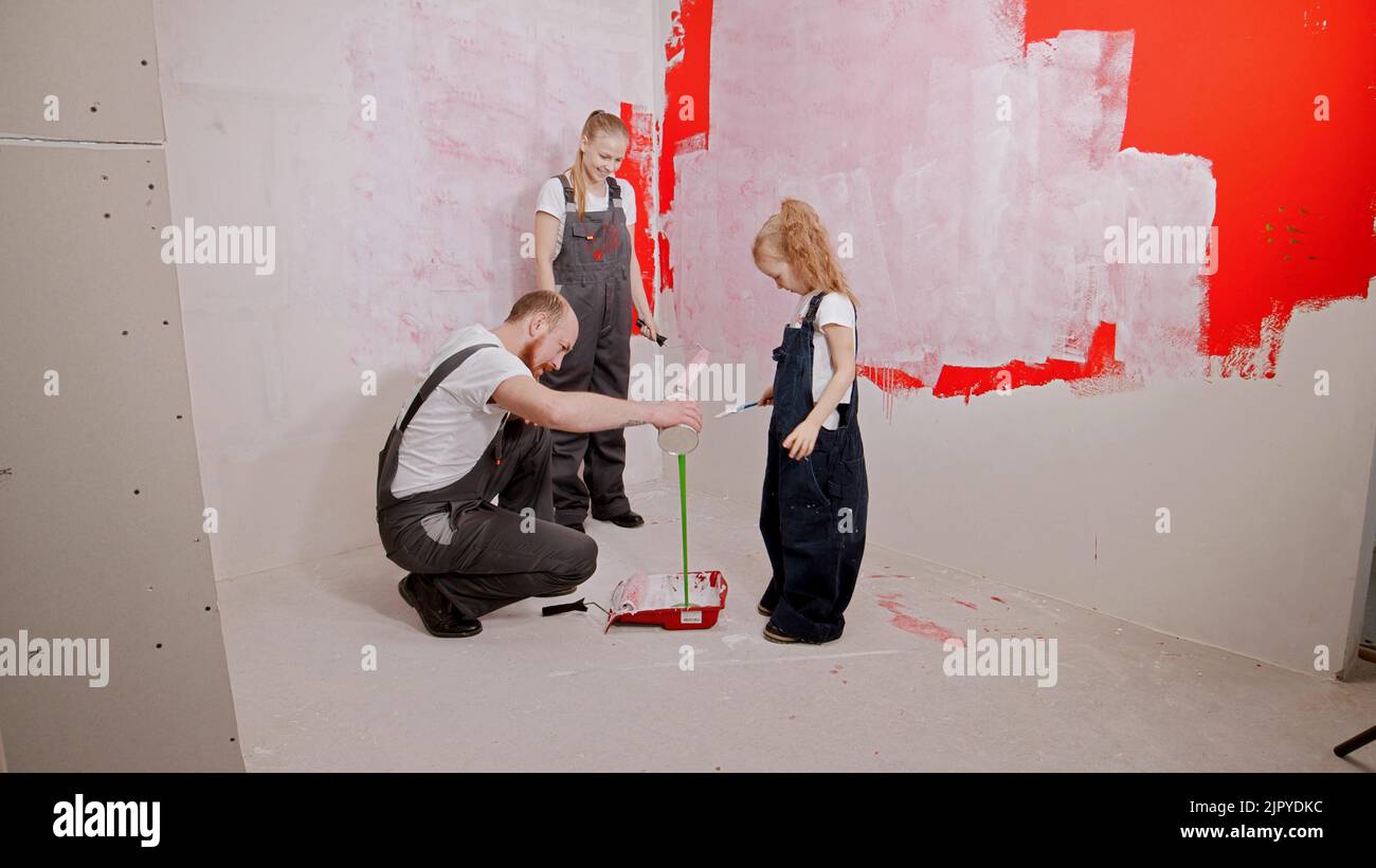 Mom and daughter are watching as the father is pouring green paint into the tray Stock Photo