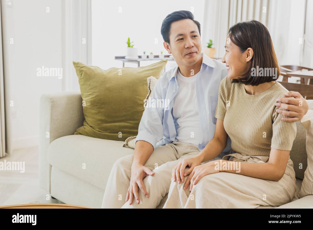 Cheerful Asian family embracing and laughing while relaxing on couch in living room. Happy parents  posing on sofa at home, spending weekend together Stock Photo
