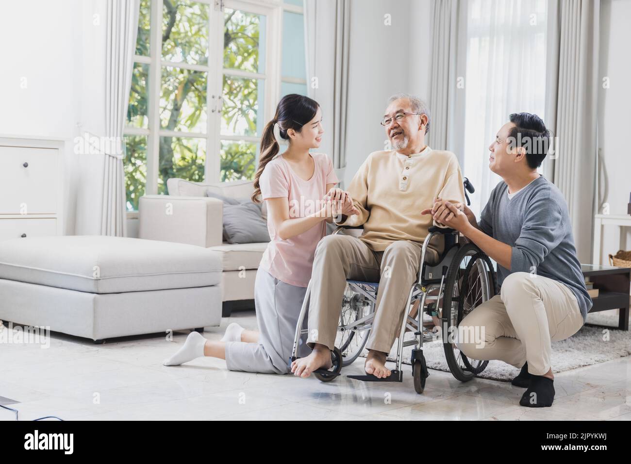 Happy family of senior with beautiful daughter and her husband, take care old man sitting on wheelchair in house, positive dad have strength and posit Stock Photo