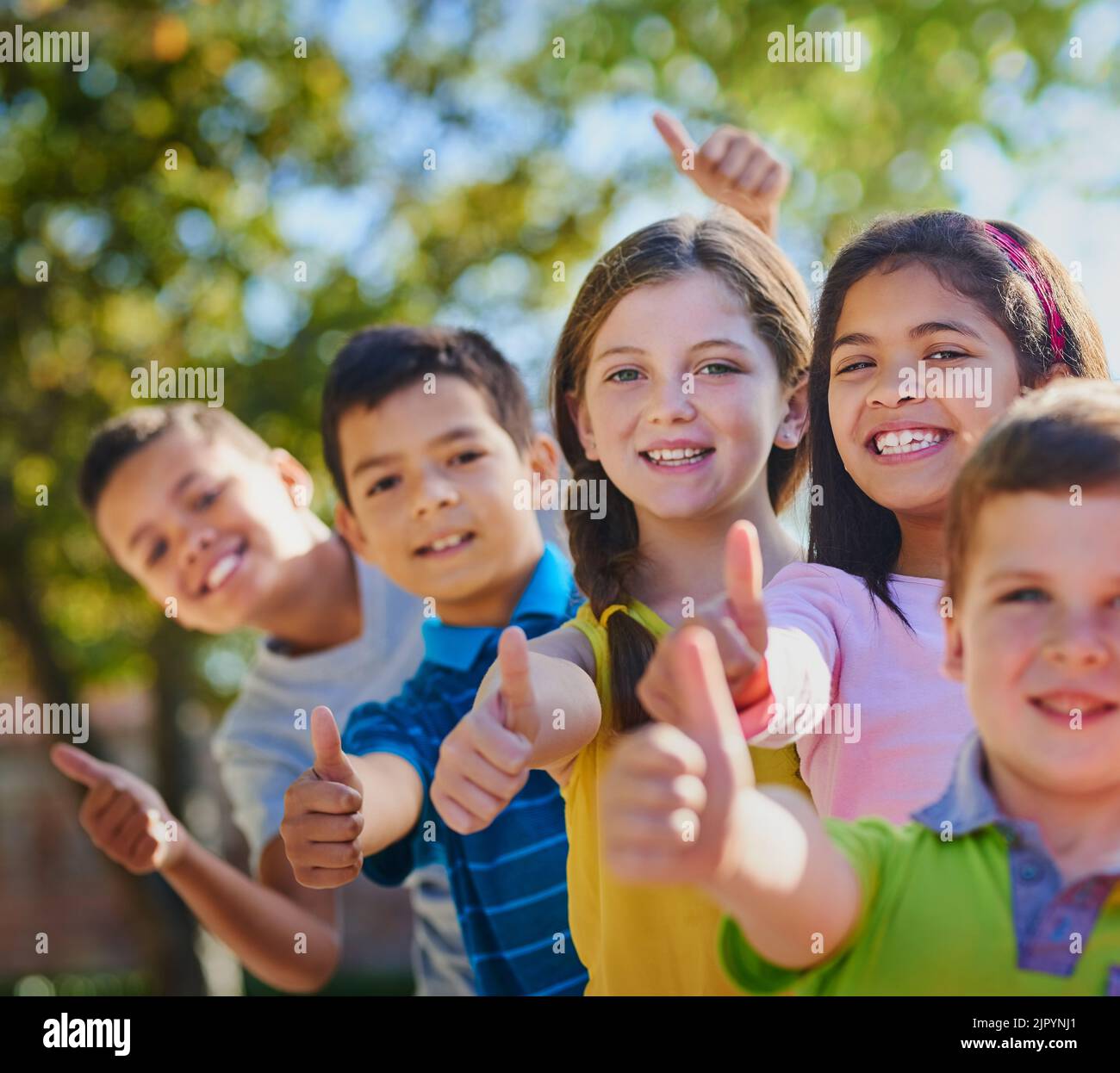 Thumbs up to being a kid. a diverse group of children showing thumbs up outside. Stock Photo