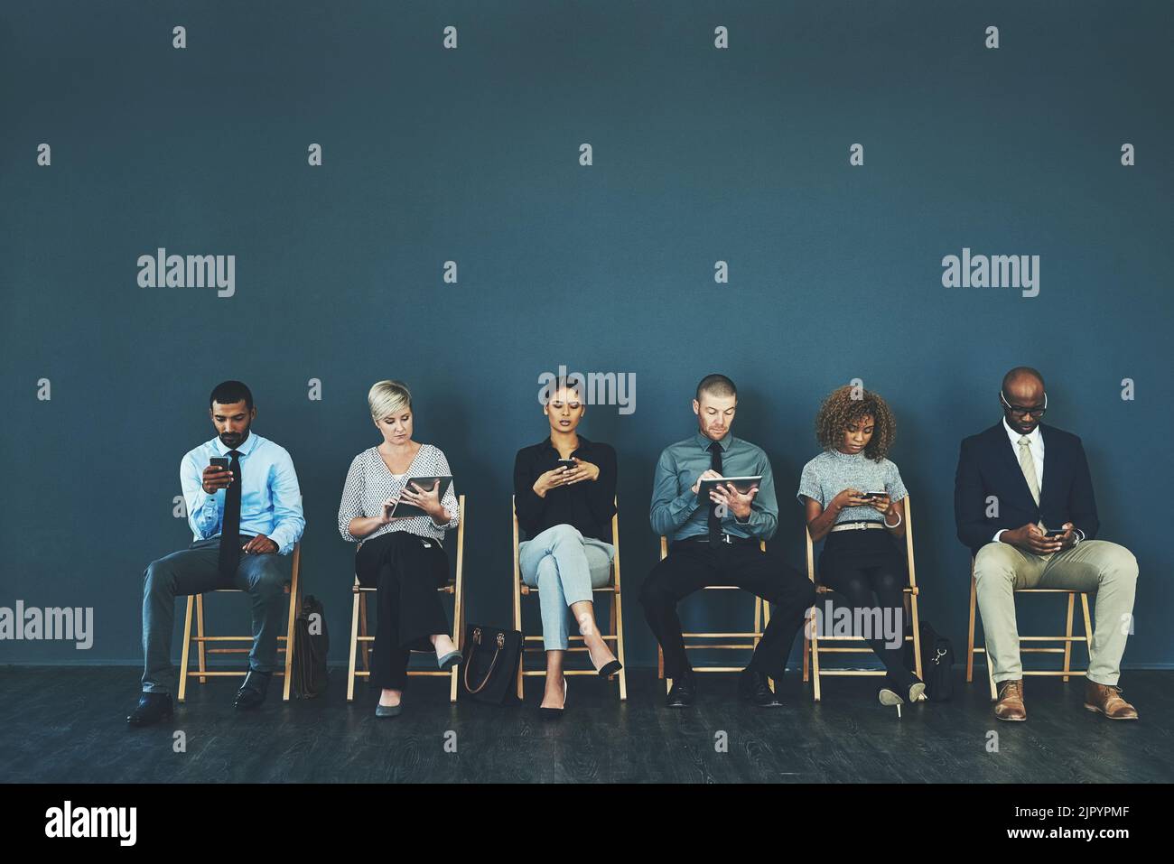 Sit tight and rehearse your answers to possible interview questions. a group of business people using their smart devices while waiting to be Stock Photo