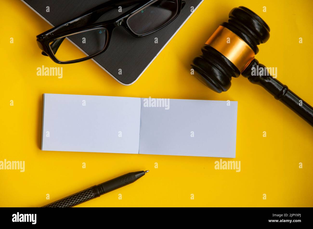 Top view of blank paper note with gavel, laptop, glasses and pen on yellow background. Copy space. Stock Photo