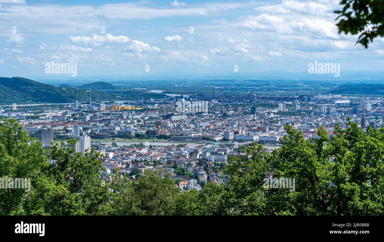 Panoramic view of Linz from Pöstlingberg, showing the city's rooftops, the Danube River winding through, and distant hills.