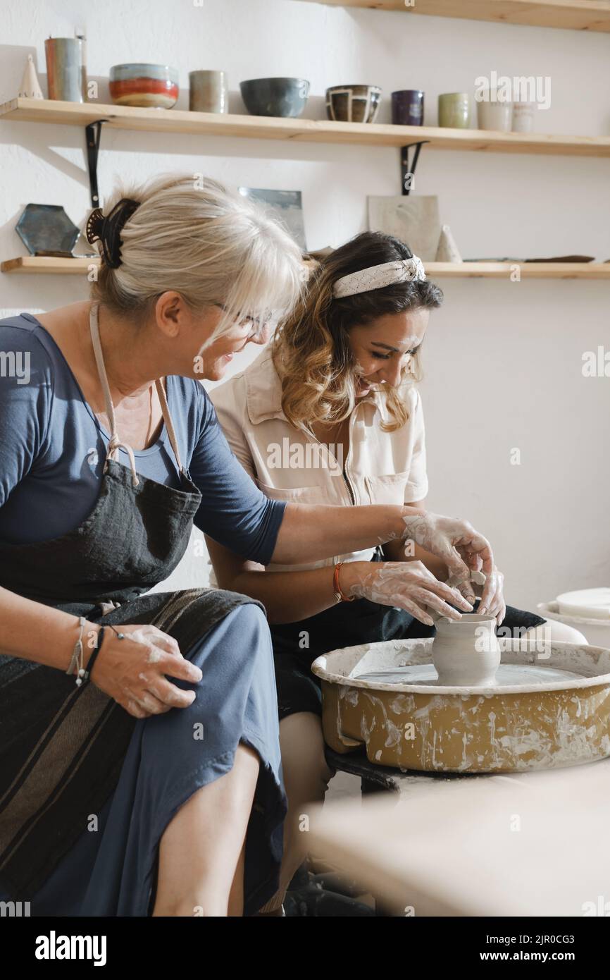 Teacher and student at pottery workshop learning to make bowls from clay. Happy woman doing handmade dishes. Lesson for adults at ceramics studio Stock Photo