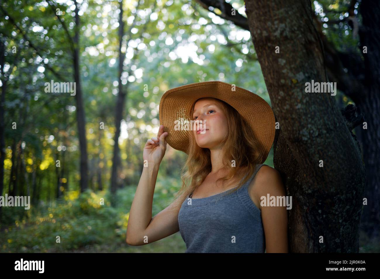 Closeup portrait of a young longhair girl in a straw hat who walks in the park or forest. Blurred nature background. Stock Photo