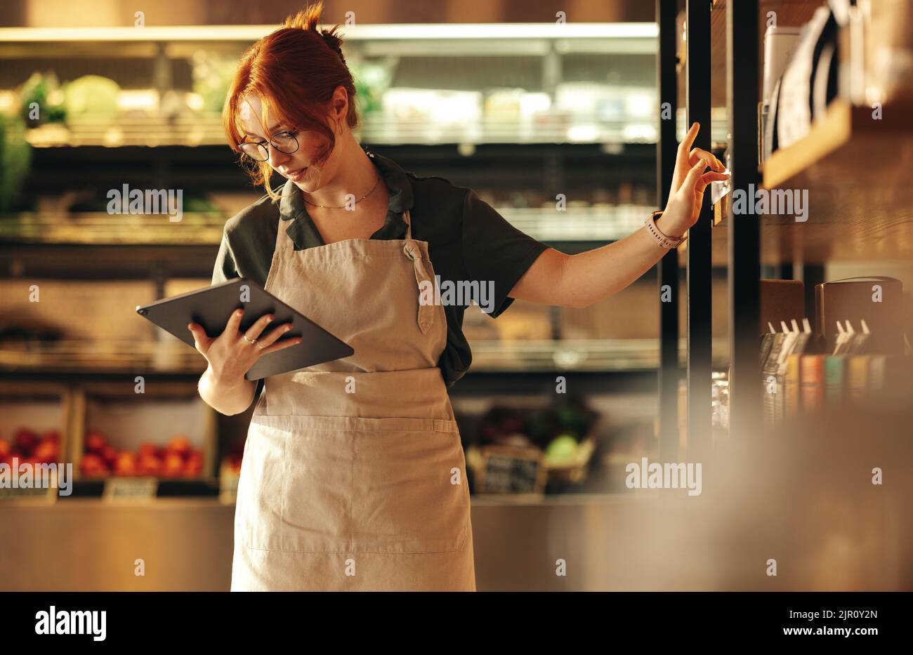 Female supermarket owner using a digital tablet while standing in her shop. Young female entrepreneur running her small business using wireless techno Stock Photo