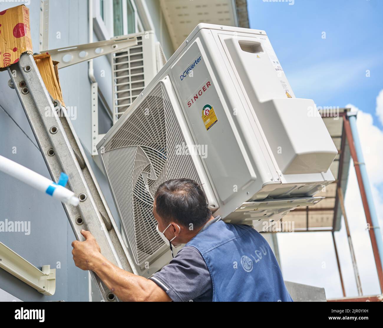 A man carries a heavy air conditioner compressor on his shoulder while climbing a ladder. Stock Photo
