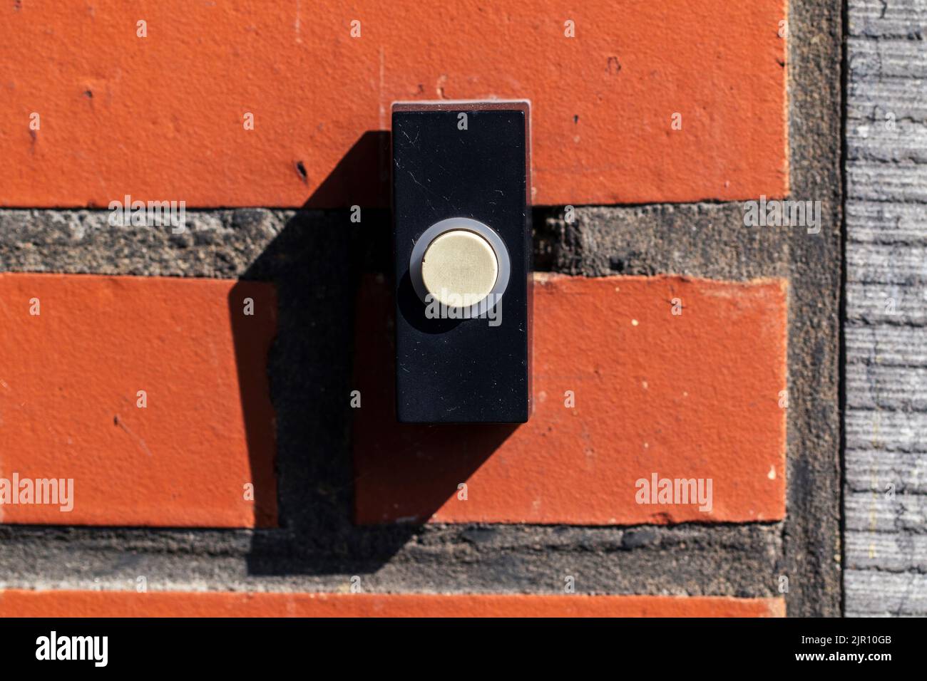 A close up portrait of an old black doorbell with a white button on a red brick wall, ready to be pressed to ring the bell and notify the residents. Stock Photo