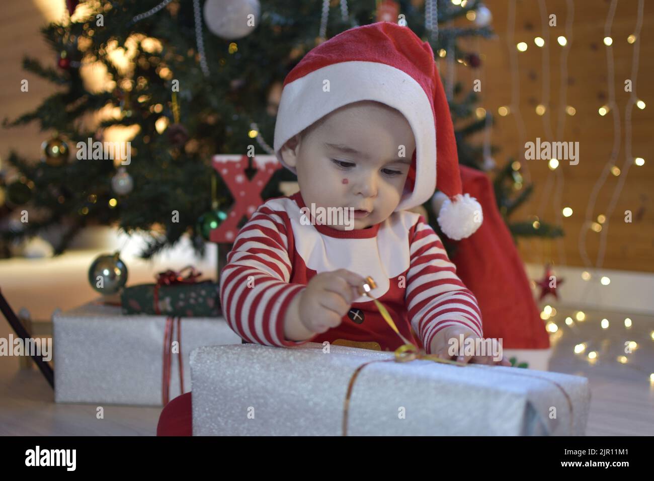 Twelve months old baby opening a Christmas gift. baby dressed as santa claus opening gift. cute