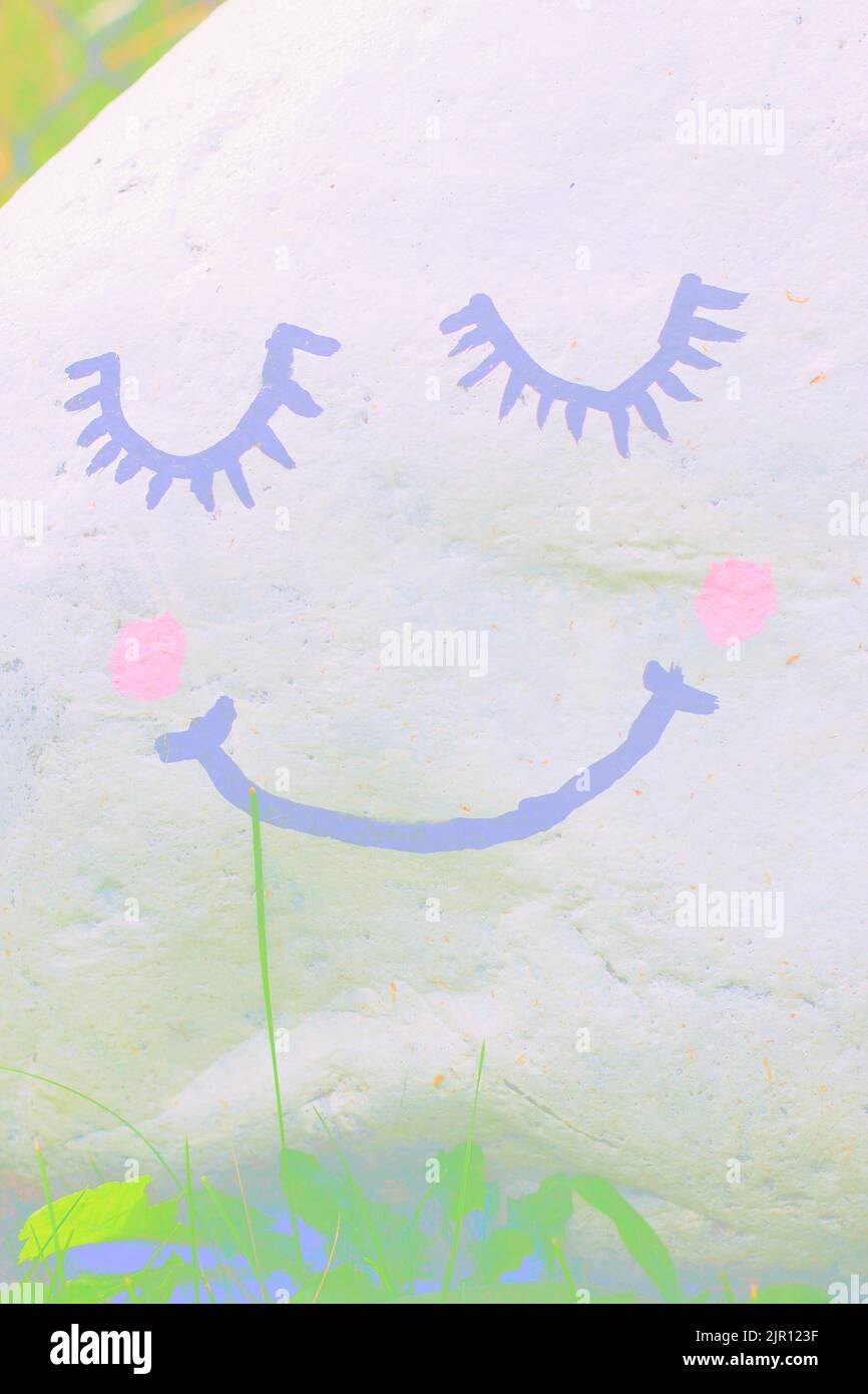 Happy smiley face painted on a garden rock as an inspirational message in a faded faint view