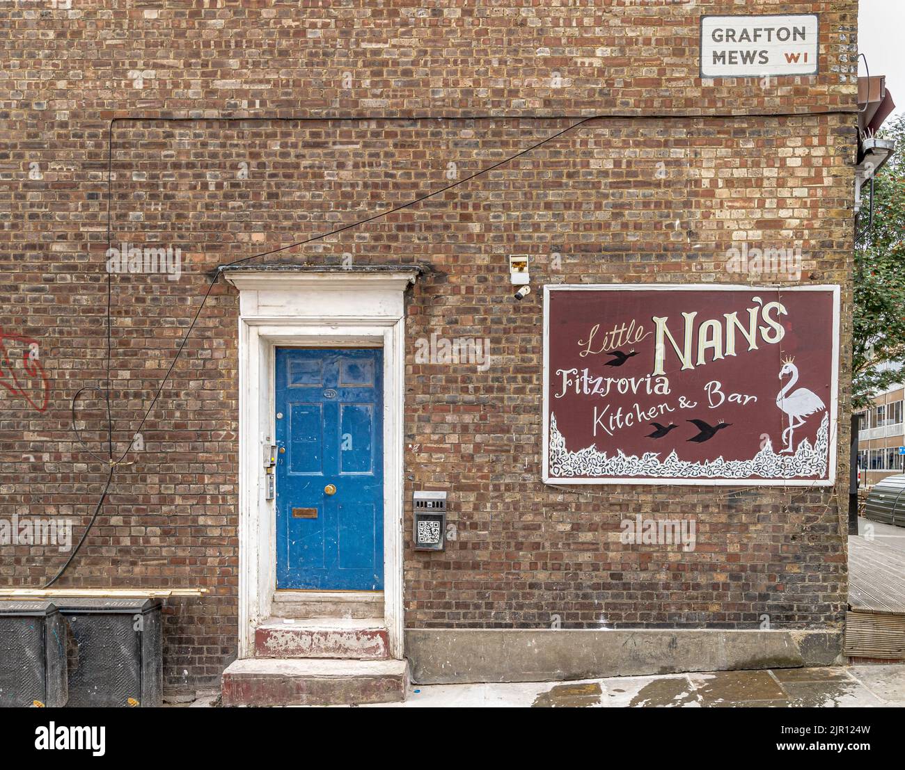 A blue door and door step with a sign for Little Nan's Kitchen & Bar on the side of a brick building wall on Grafton Mews, Fitzrovia, London W1 Stock Photo