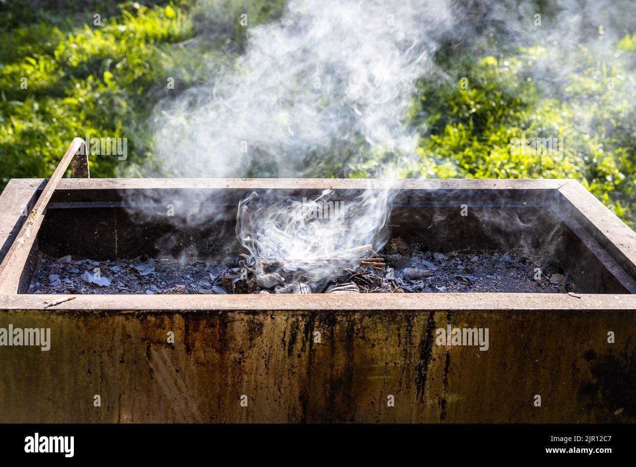 smoke over flaming pile of wood chips in backyard barbecue on sunny summer evening Stock Photo