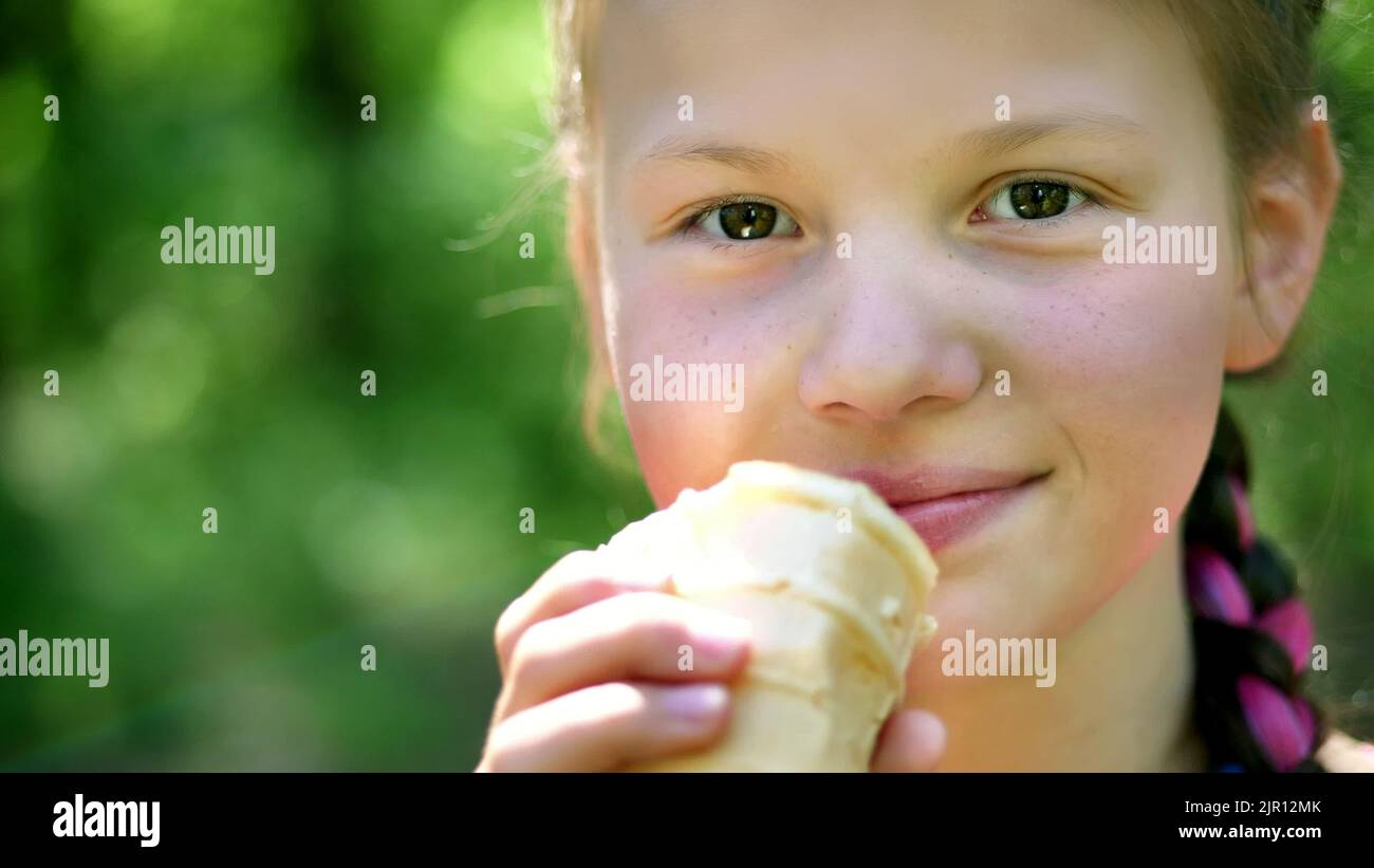 portrait, pretty girl of eight years, blonde, with freckles, eating white ice cream in a waffle cup, licks it with tongue. summer. High quality photo Stock Photo