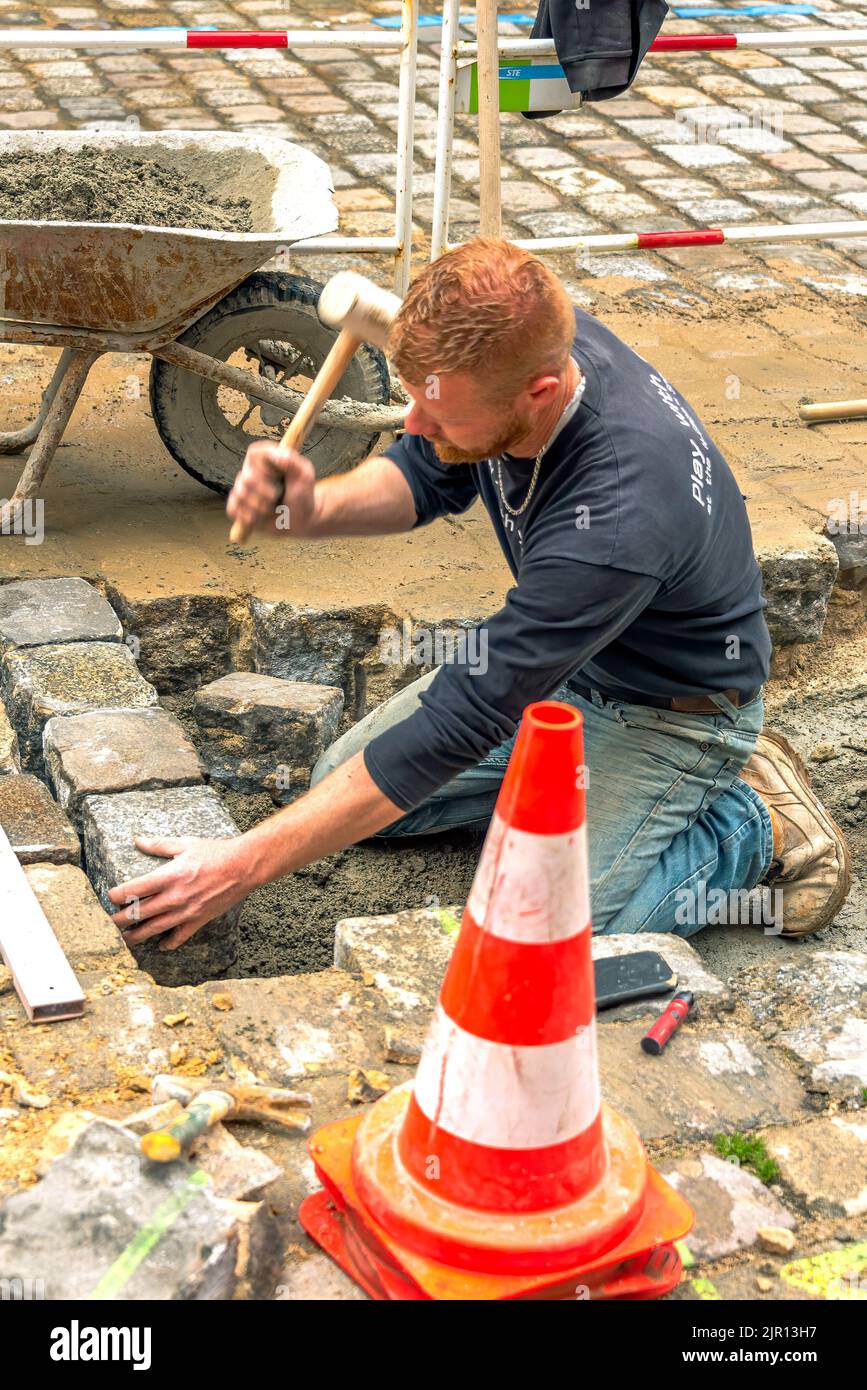 Dinan, France – April 12, 2022: Cobblestone Street. A  worker is re-paving of quarried stone on the driveway. Stock Photo
