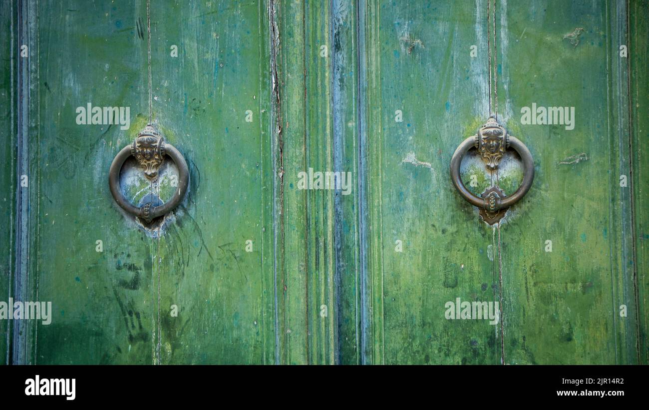 Old and worn double-leaf door with metal knockers and painted dark green Stock Photo