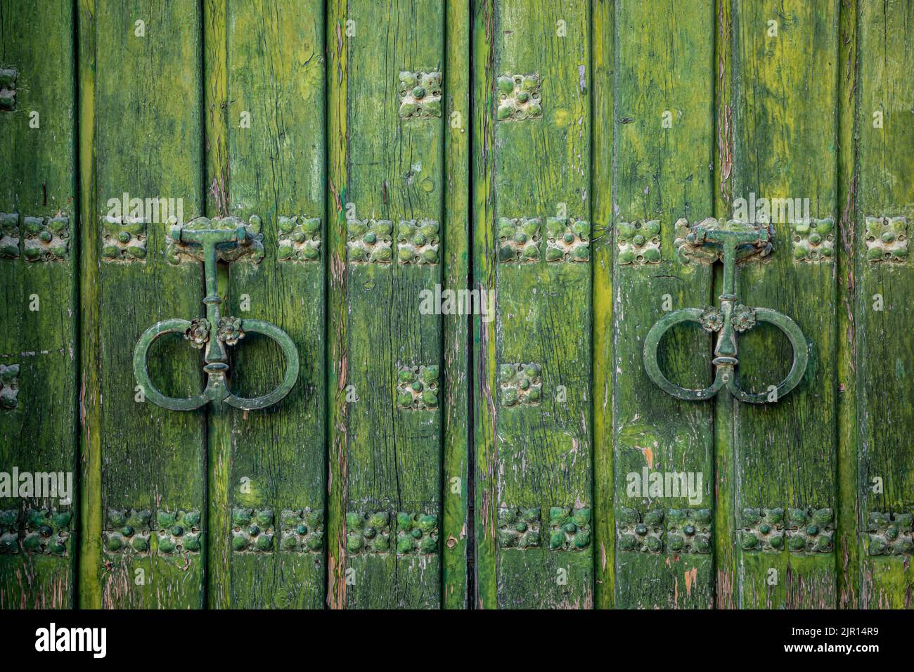 Old and worn double-leaf door with metal knockers and painted dark green Stock Photo