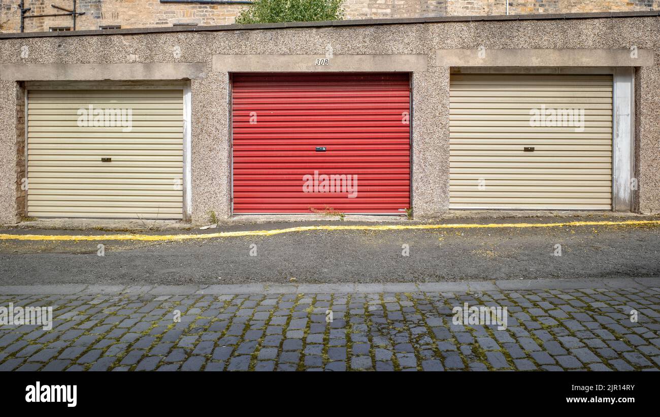 Odd Man Out - three garages in a row, two white and one red, on a cobbled street in Edinburgh, UK. Stock Photo