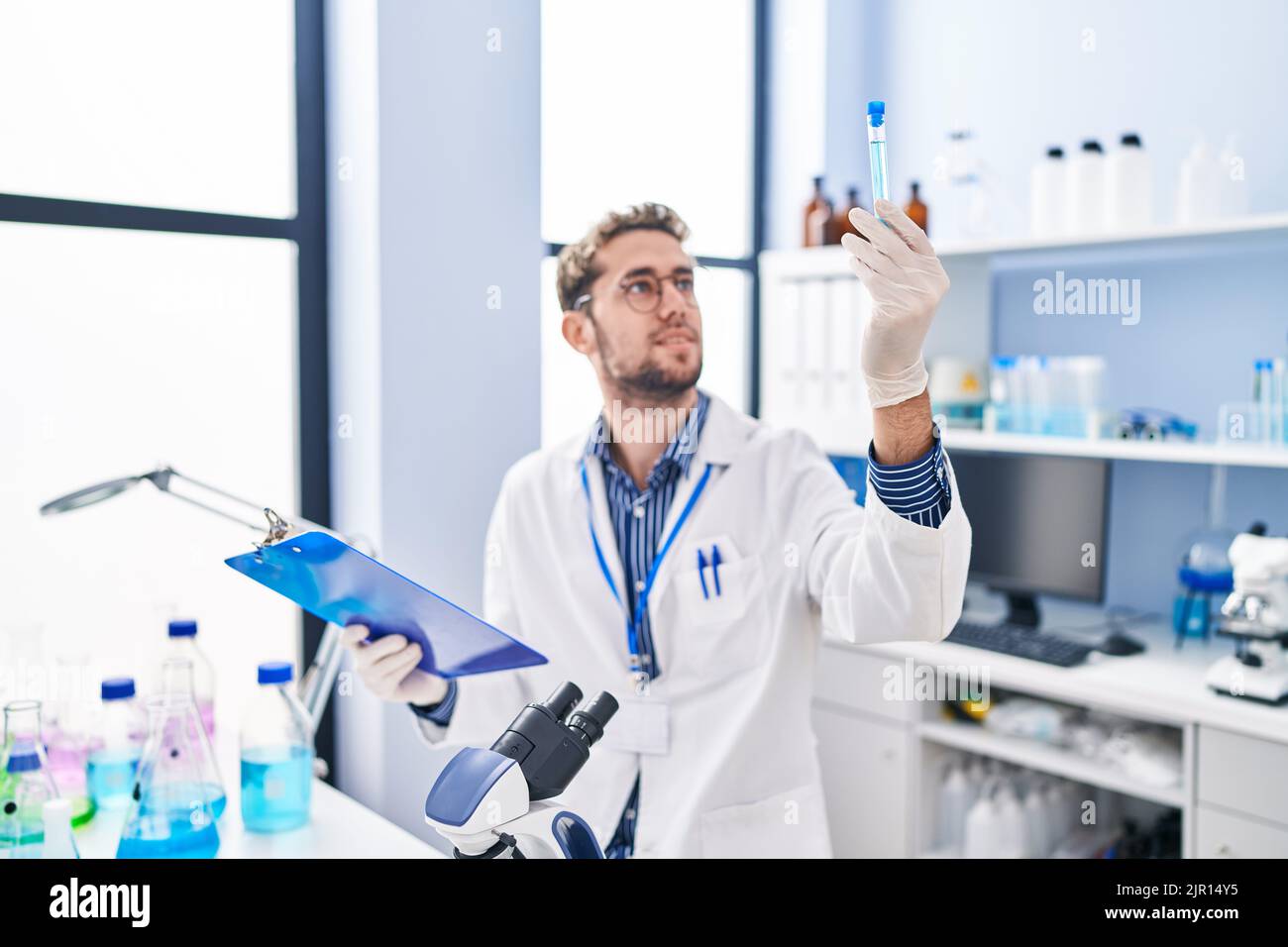 Young man scientist reading report holding test tube at laboratory ...