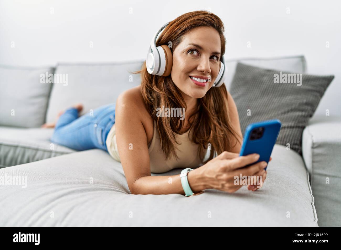 Young latin woman listening to music lying on sofa at home Stock Photo ...